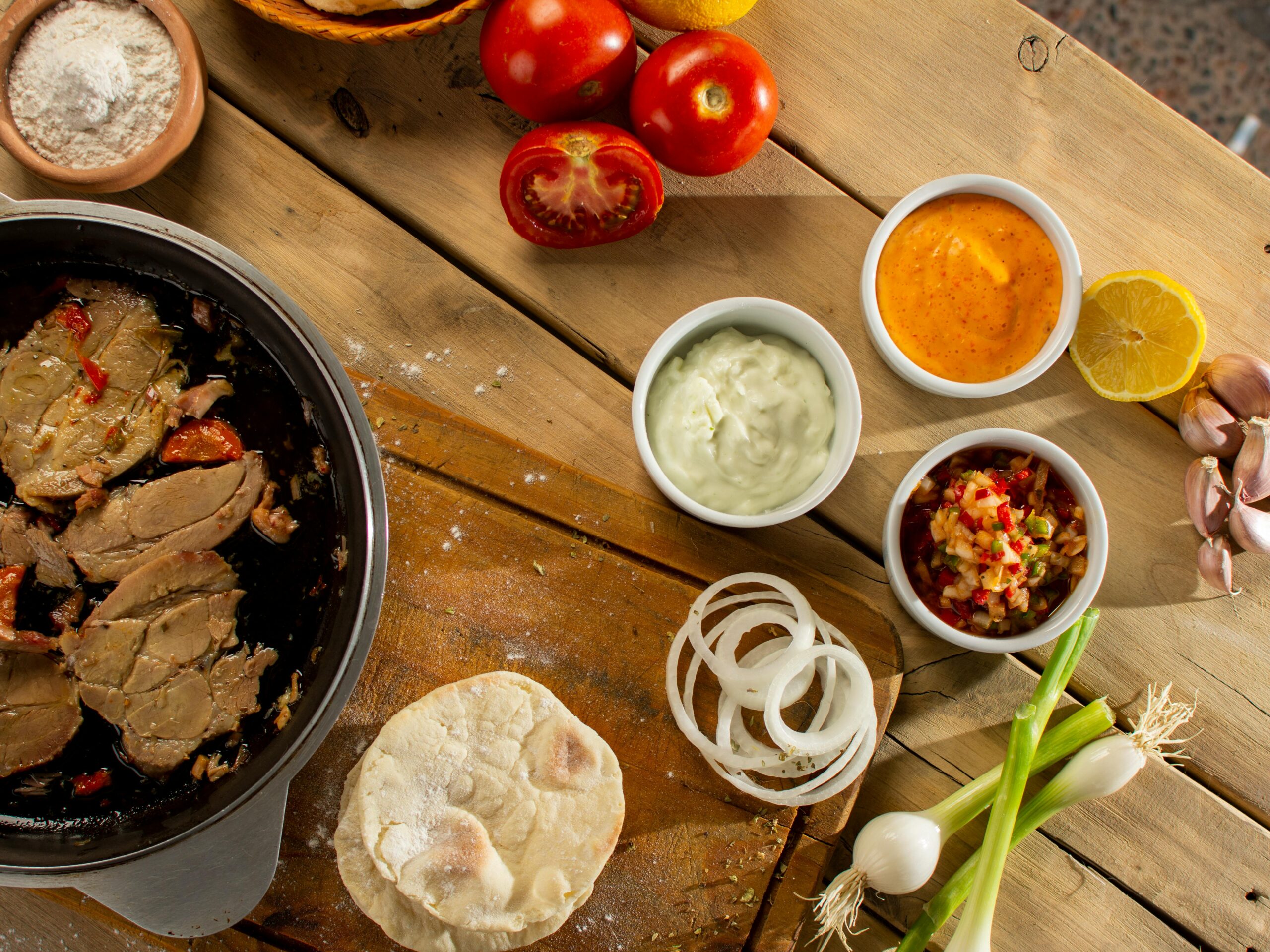 Aerial view of a kitchen table with ingredients, sauces, and cooked meat for a meal preparation.